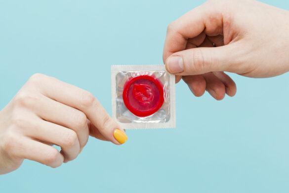 Tipos de DST: foto de duas mãos (uma de um homem e outra de uma mulher) segurando um preservativo vermelho